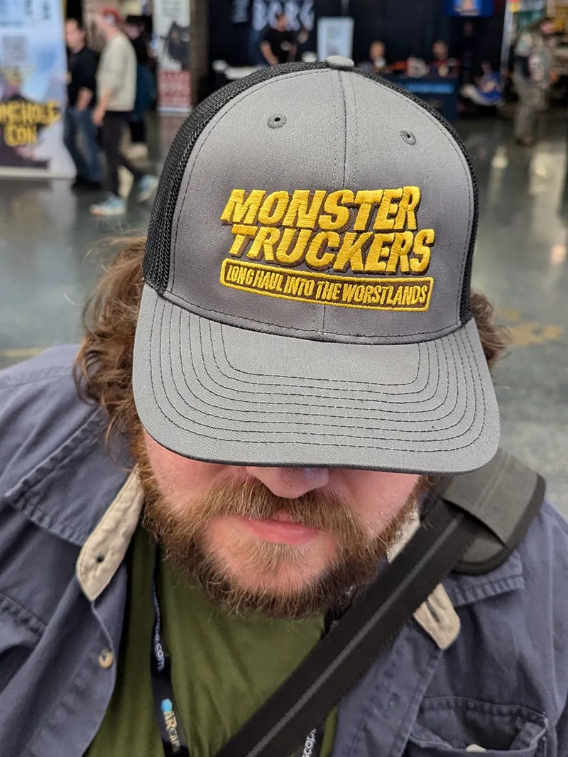 Image focusing on a Monster Truckers hat on a man's head.